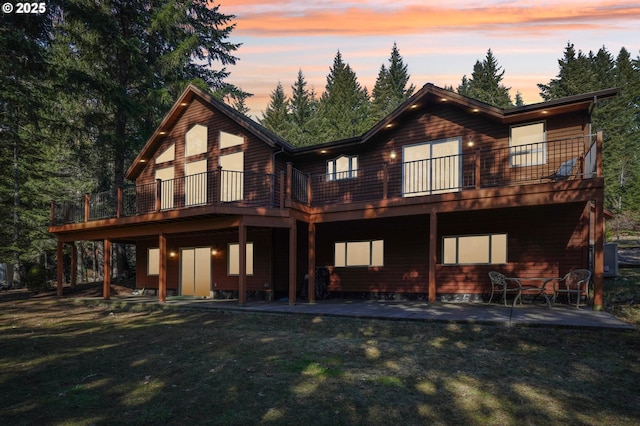 back of property at dusk featuring a patio, a lawn, and a deck