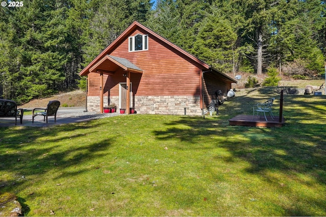 view of side of home with stone siding, a wooden deck, a wooded view, and a yard