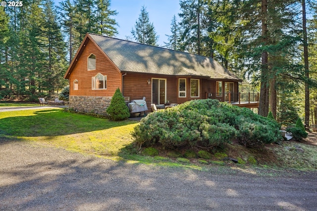 chalet / cabin with stone siding, a front lawn, and roof with shingles