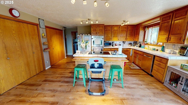 kitchen with brown cabinetry, a center island, tile countertops, light wood-style flooring, and stainless steel appliances