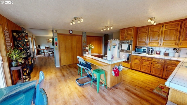 kitchen with a kitchen island, tile countertops, a textured ceiling, light wood-style flooring, and stainless steel appliances