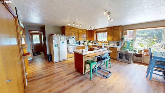 kitchen featuring brown cabinetry, a kitchen island, white refrigerator with ice dispenser, double oven, and light wood-style flooring