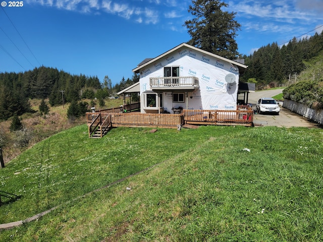 back of house featuring a view of trees, a yard, a deck, and a balcony