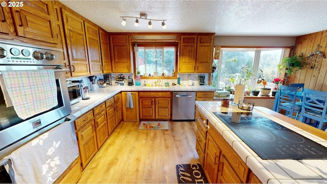 kitchen featuring a textured ceiling, tile countertops, light wood-style flooring, and dishwasher