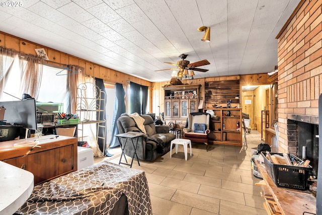 living room with wooden walls, ceiling fan, a fireplace, and light tile patterned floors