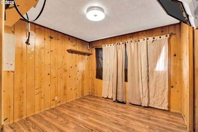 empty room featuring wooden walls, wood finished floors, and a textured ceiling