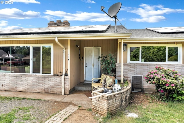doorway to property featuring solar panels, a chimney, stone siding, and a shingled roof