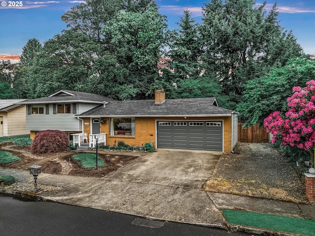 tri-level home featuring brick siding, a garage, a chimney, driveway, and fence