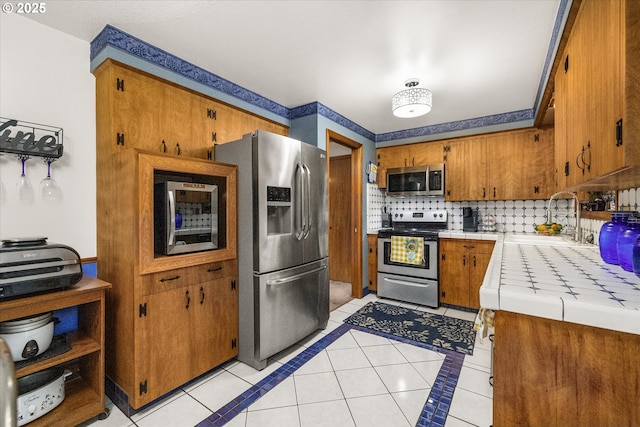 kitchen with appliances with stainless steel finishes, tile counters, a sink, and light tile patterned floors