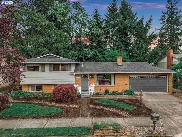 split level home with brick siding, concrete driveway, a garage, a chimney, and a shingled roof
