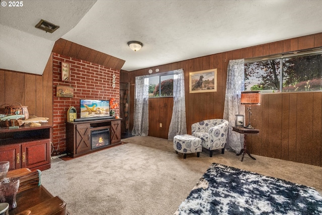 carpeted living room featuring wood walls, a textured ceiling, and a fireplace