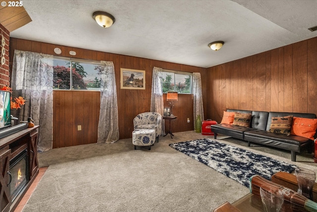 living room with carpet flooring, wooden walls, a textured ceiling, and a glass covered fireplace
