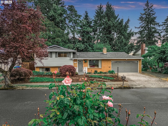 split level home featuring brick siding, a garage, driveway, and a chimney