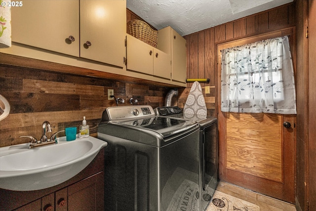washroom with wood walls, washer and clothes dryer, cabinet space, a textured ceiling, and light tile patterned floors
