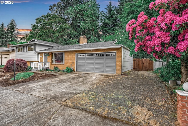 split level home featuring fence, an attached garage, a chimney, and brick siding