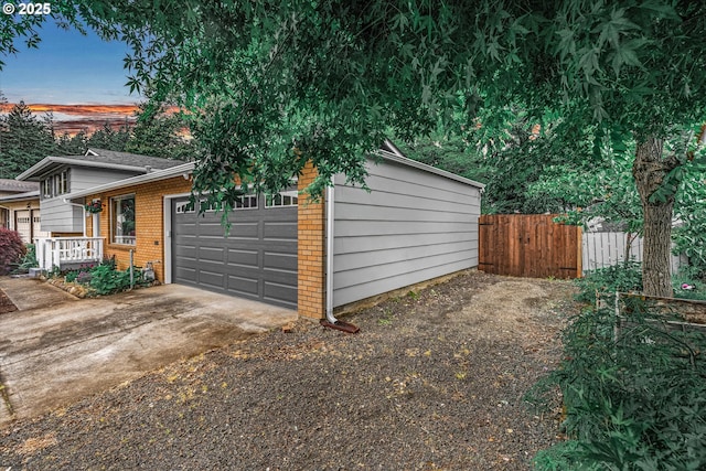 view of side of home featuring fence, an attached garage, brick siding, and concrete driveway