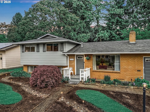 tri-level home featuring a chimney, brick siding, and roof with shingles