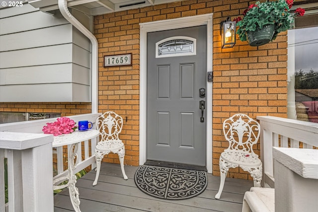 doorway to property featuring a porch and brick siding