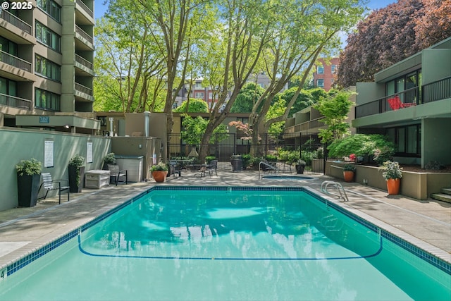 community pool featuring fence, a patio, and a hot tub