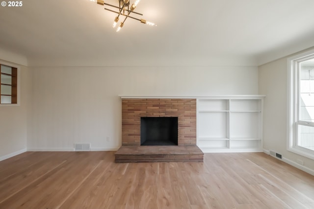 unfurnished living room with an inviting chandelier, visible vents, wood finished floors, and baseboards
