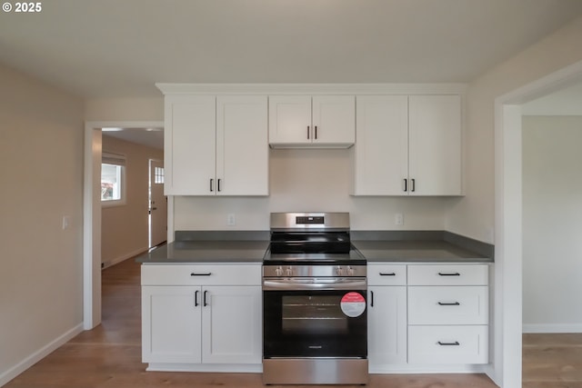 kitchen with baseboards, stainless steel electric stove, dark countertops, and white cabinetry