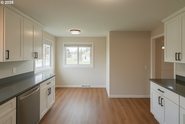 kitchen featuring visible vents, stainless steel dishwasher, light wood-style floors, and dark countertops