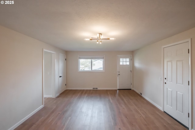 foyer with an inviting chandelier, visible vents, light wood-type flooring, and baseboards