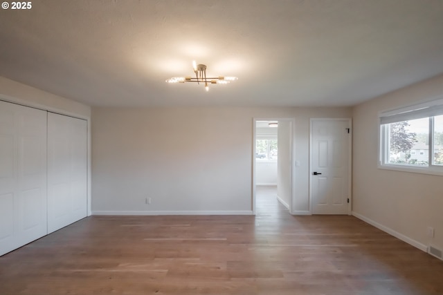 unfurnished bedroom with multiple windows, baseboards, a chandelier, and light wood-type flooring