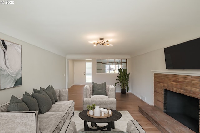 living room with a chandelier, wood finished floors, and a fireplace with raised hearth