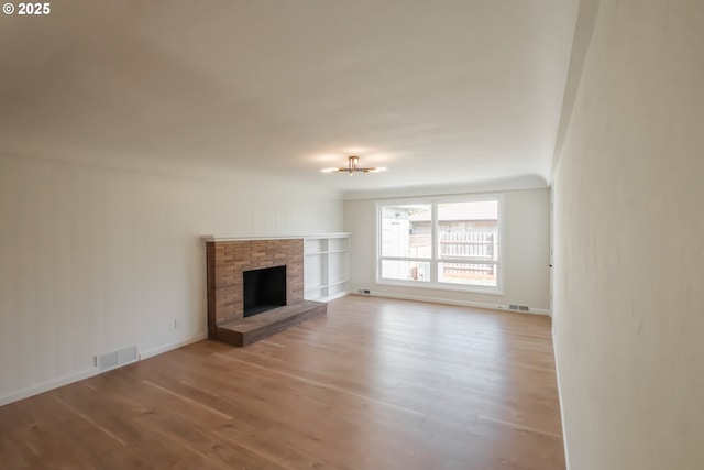 unfurnished living room featuring a fireplace with raised hearth, visible vents, wood finished floors, and baseboards