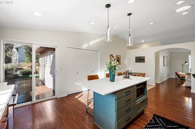 kitchen featuring arched walkways, stainless steel microwave, a breakfast bar, and dark wood-style flooring