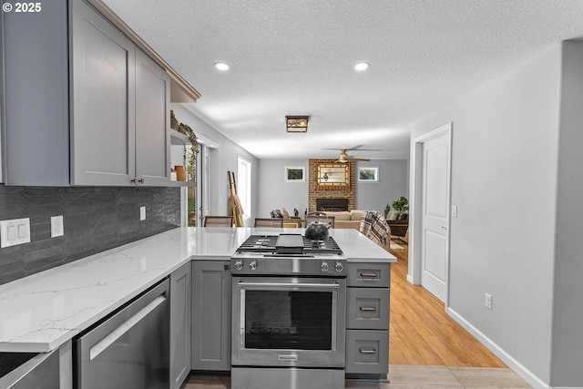 2111 NE 149th Ave, Vancouver, WA 98684 - kitchen featuring gray cabinets, stainless steel appliances, a peninsula, a brick fireplace, and decorative backsplash