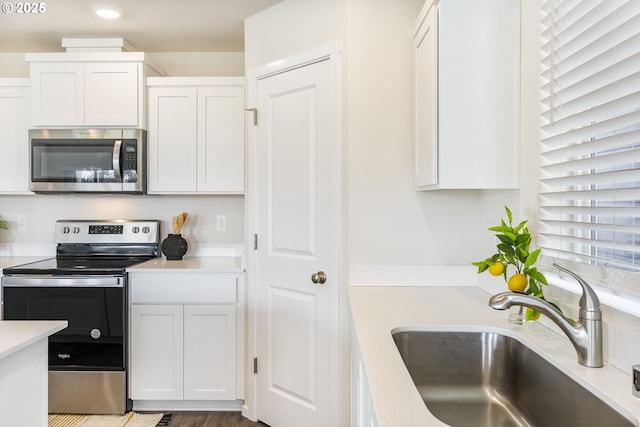 kitchen with stainless steel appliances, light countertops, white cabinets, and a sink