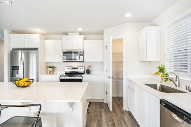 kitchen featuring dark wood-type flooring, a sink, a kitchen breakfast bar, white cabinets, and appliances with stainless steel finishes