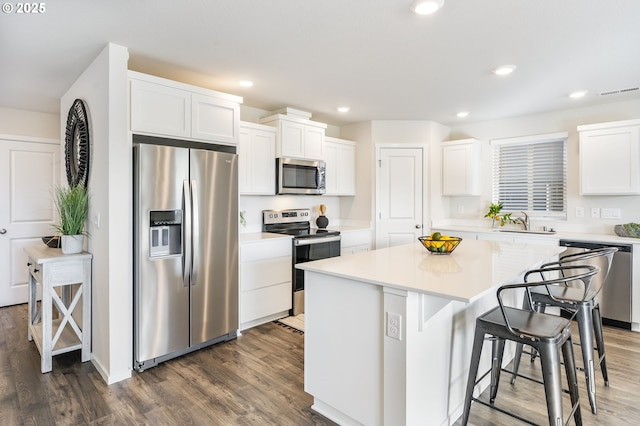 kitchen featuring dark wood-style floors, a center island, appliances with stainless steel finishes, white cabinets, and a kitchen bar