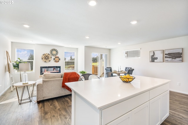 kitchen featuring dark wood-type flooring, a glass covered fireplace, a wealth of natural light, and a center island