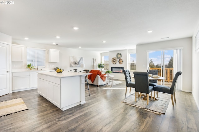 kitchen featuring recessed lighting, wood finished floors, a kitchen island, white cabinetry, and a glass covered fireplace