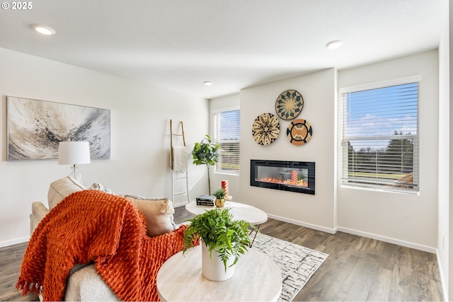 living room featuring a glass covered fireplace, recessed lighting, baseboards, and wood finished floors