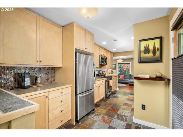 kitchen featuring light brown cabinetry, stainless steel appliances, recessed lighting, backsplash, and stone tile flooring