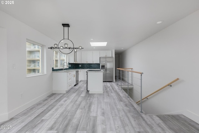 3929 NW Jetty Ave Unit 5, Lincoln City, OR 97367 - kitchen with appliances with stainless steel finishes, white cabinetry, a skylight, backsplash, and light wood-type flooring