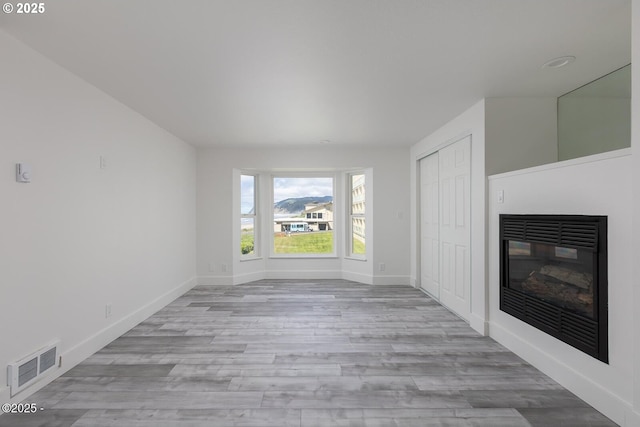 3929 NW Jetty Ave Unit 5, Lincoln City, OR 97367 - unfurnished living room featuring a glass covered fireplace, light wood-style flooring, and baseboards