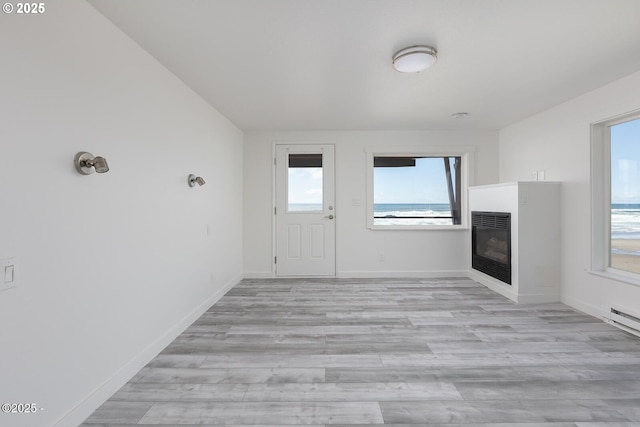 3929 NW Jetty Ave Unit 5, Lincoln City, OR 97367 - unfurnished living room with a glass covered fireplace, light wood-type flooring, and baseboards