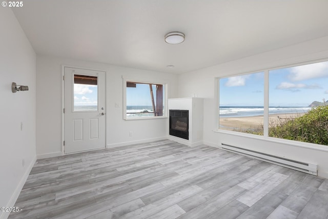 3929 NW Jetty Ave Unit 5, Lincoln City, OR 97367 - unfurnished living room featuring baseboard heating, light wood finished floors, a glass covered fireplace, and baseboards