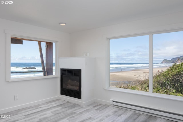 3929 NW Jetty Ave Unit 5, Lincoln City, OR 97367 - unfurnished living room featuring a baseboard radiator, a glass covered fireplace, baseboards, light wood-style floors, and view of water and beach