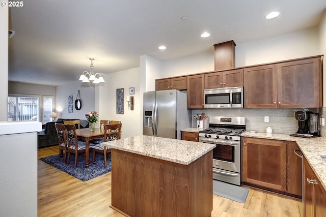 kitchen featuring stainless steel appliances, light wood-style floors, backsplash, a chandelier, and a center island