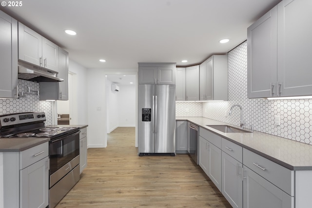 kitchen featuring light wood-style flooring, appliances with stainless steel finishes, a sink, under cabinet range hood, and backsplash