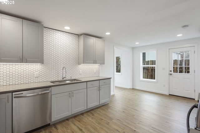 kitchen featuring decorative backsplash, gray cabinetry, light wood-type flooring, stainless steel dishwasher, and a sink