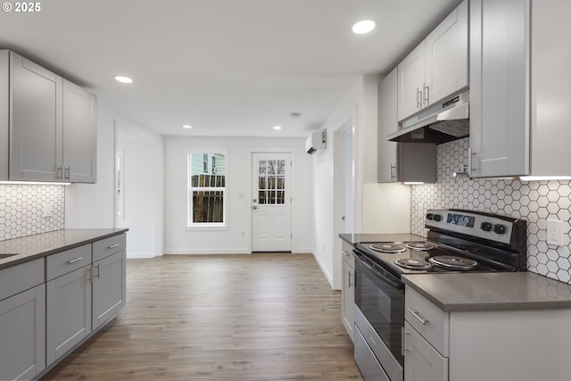 kitchen with baseboards, stainless steel electric range oven, light wood-type flooring, under cabinet range hood, and recessed lighting