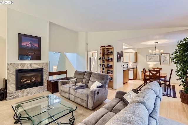 living room featuring a notable chandelier, vaulted ceiling, a premium fireplace, and light wood-type flooring