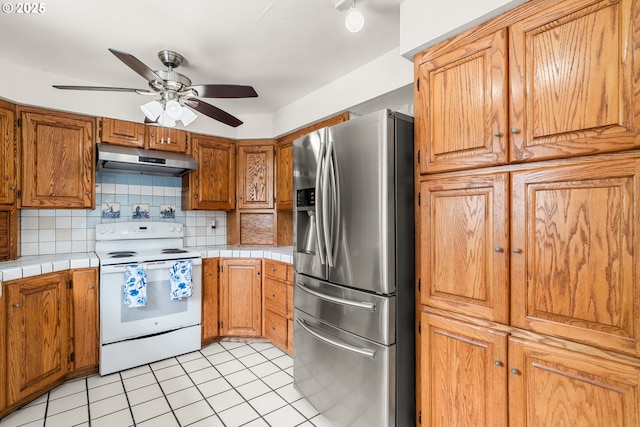 409 Pacific Ave, Brookings, OR 97415 - kitchen with stainless steel refrigerator with ice dispenser, white range with electric cooktop, under cabinet range hood, a ceiling fan, and tile counters